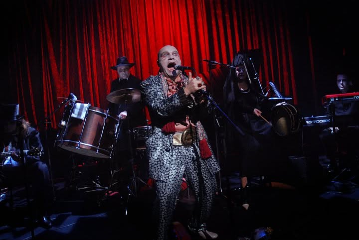 Voodoo Explosion musicians performing before a red curtain